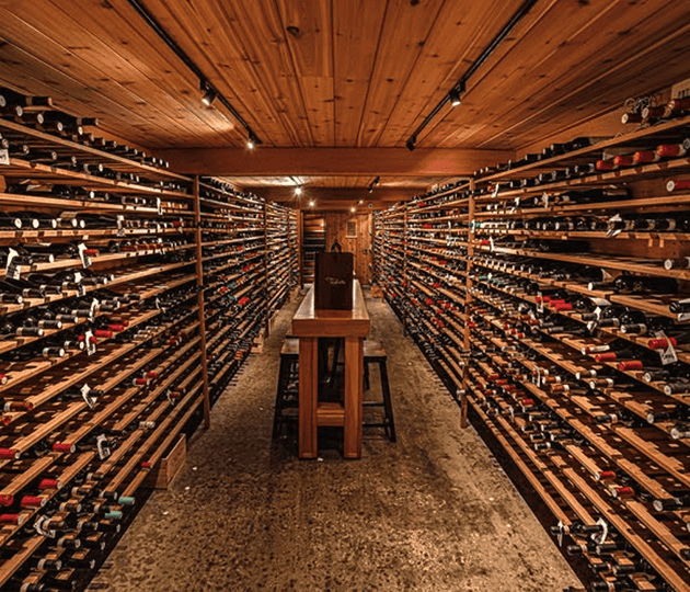 A wine cellar with wooden shelves filled with bottles of wine on both sides and a wooden table in the center.